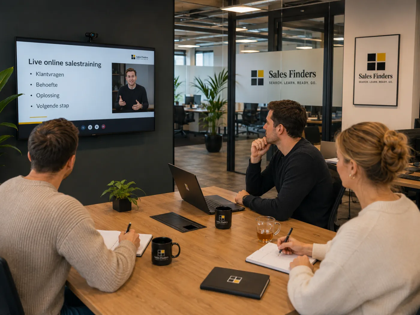 Drie deelnemers volgen een live online salestraining op het scherm in de vergaderruimte en maken aantekeningen.