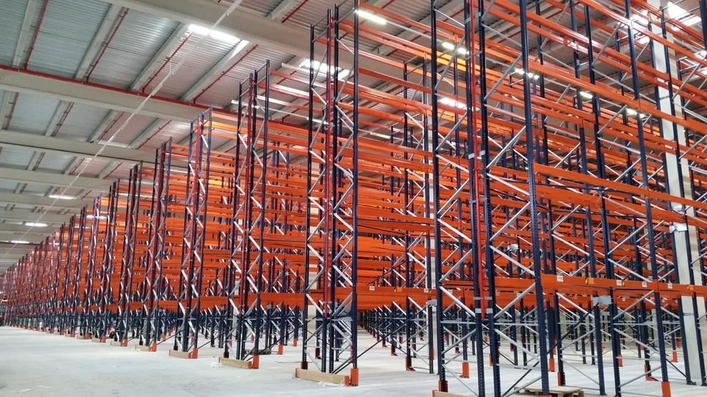 Rijen hoge magazijnstellingen in een leeg distributiecentrum, oranje en blauw geschilderd.